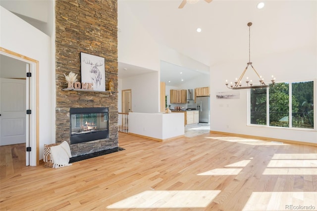 unfurnished living room with a chandelier, a high ceiling, a stone fireplace, light wood-style flooring, and baseboards