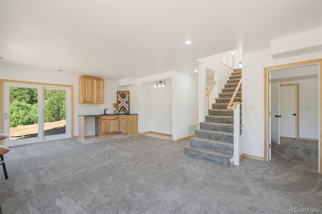 unfurnished living room featuring light carpet, stairs, baseboards, recessed lighting, and bar with sink