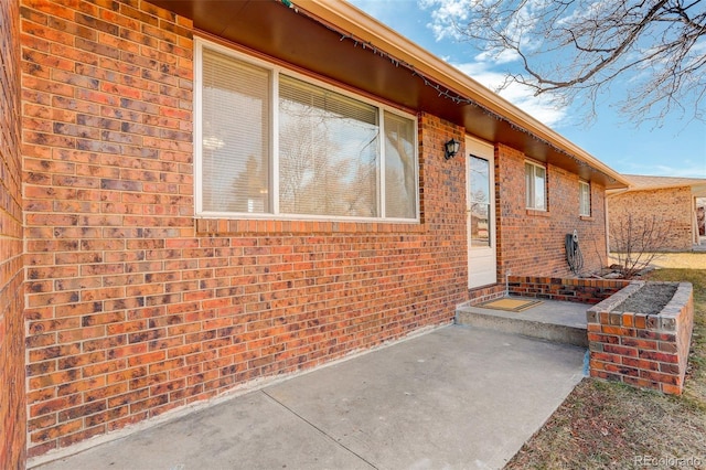 view of exterior entry with brick siding and a patio area