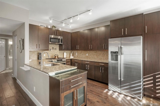 kitchen featuring appliances with stainless steel finishes, dark brown cabinetry, light stone countertops, dark hardwood / wood-style flooring, and kitchen peninsula