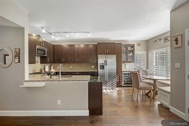 kitchen featuring sink, appliances with stainless steel finishes, dark brown cabinets, light stone countertops, and light wood-type flooring