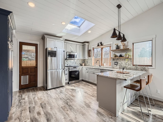 kitchen with tasteful backsplash, light wood-style flooring, appliances with stainless steel finishes, a peninsula, and light stone countertops