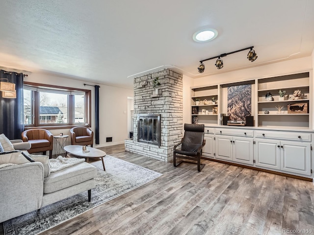 living room featuring a stone fireplace, light wood finished floors, and a textured ceiling