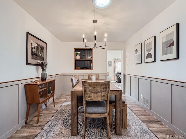 dining area with a notable chandelier, wood finished floors, and a decorative wall