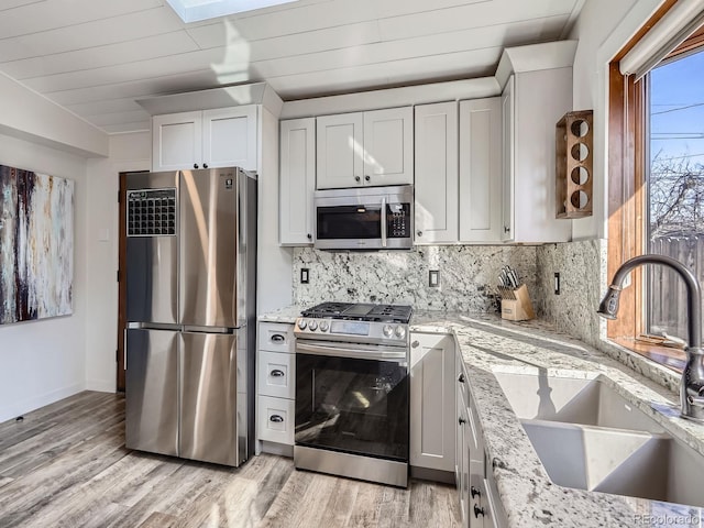 kitchen with light stone countertops, backsplash, stainless steel appliances, and a sink