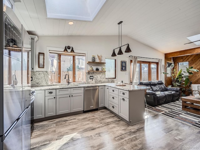 kitchen with gray cabinetry, appliances with stainless steel finishes, lofted ceiling with skylight, a sink, and a peninsula