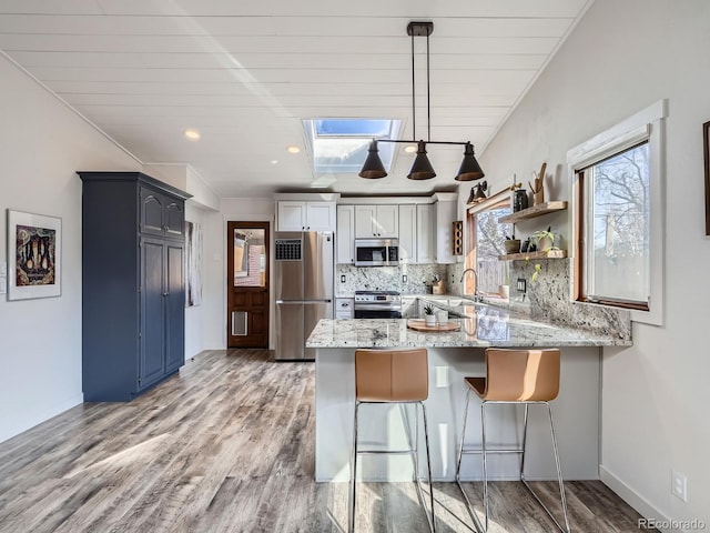 kitchen featuring a peninsula, appliances with stainless steel finishes, backsplash, light wood finished floors, and a kitchen bar