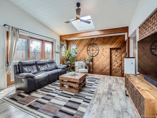 living area with a ceiling fan, vaulted ceiling with skylight, wood walls, and wood finished floors