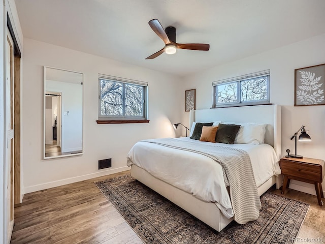 bedroom with baseboards, multiple windows, visible vents, and wood finished floors