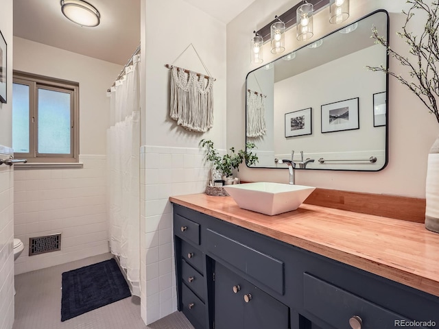 full bathroom featuring a wainscoted wall, tile walls, visible vents, vanity, and tile patterned floors