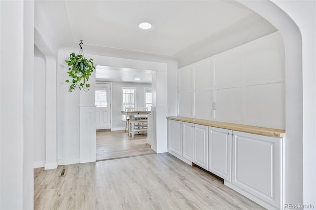 interior space with arched walkways, a decorative wall, light wood finished floors, and visible vents