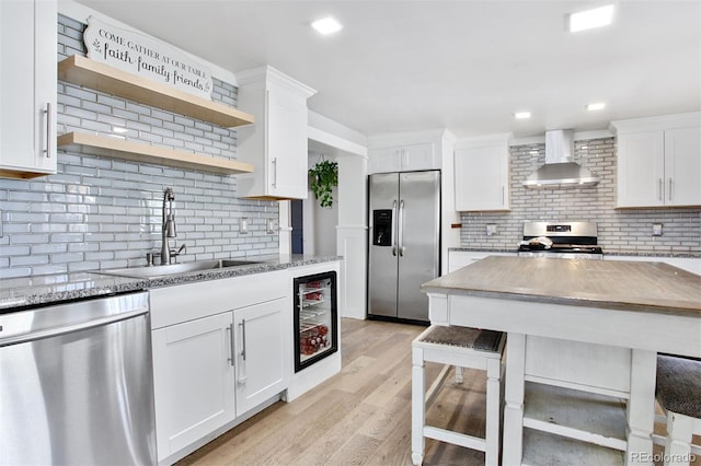 kitchen with wall chimney range hood, tasteful backsplash, open shelves, a sink, and stainless steel appliances