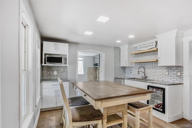 kitchen with stainless steel appliances, a sink, tasteful backsplash, white cabinetry, and beverage cooler