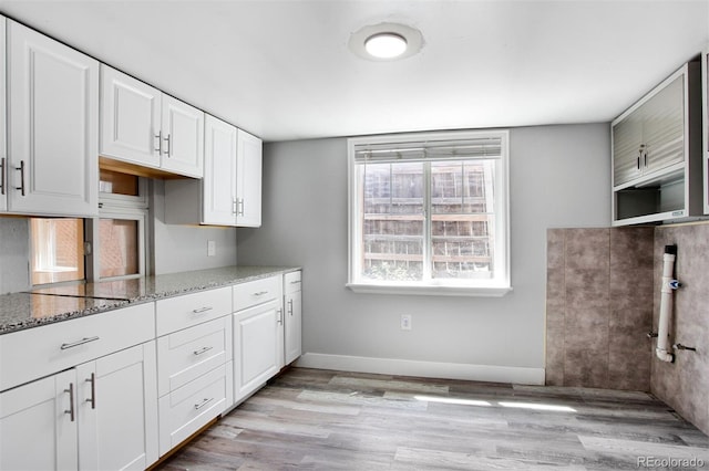 kitchen with baseboards, light stone counters, white cabinetry, and light wood-style flooring