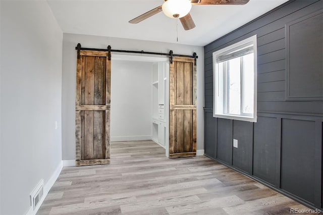 interior space featuring ceiling fan, light wood finished floors, a barn door, and visible vents