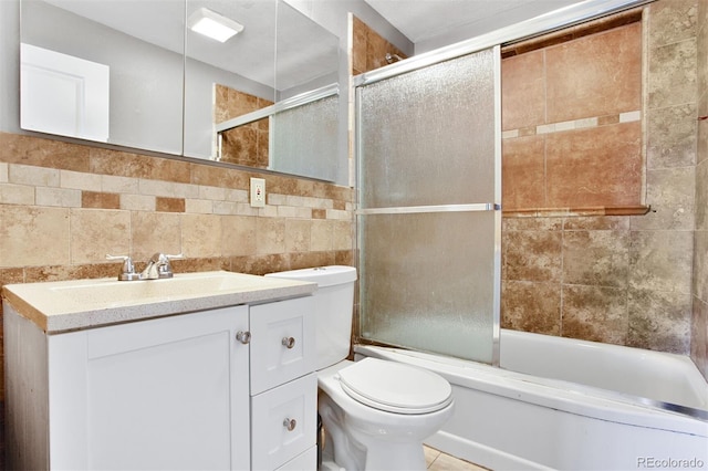 full bath with shower / bath combination with glass door, tile patterned flooring, toilet, vanity, and tile walls