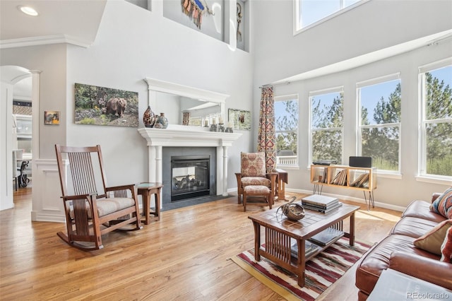 living room with arched walkways, a fireplace with flush hearth, light wood finished floors, crown molding, and a high ceiling