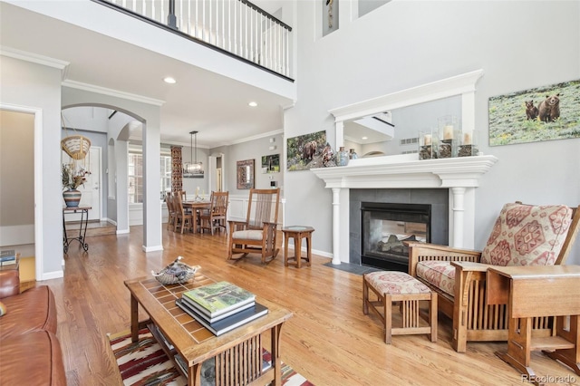living area with arched walkways, crown molding, wood finished floors, a tiled fireplace, and baseboards