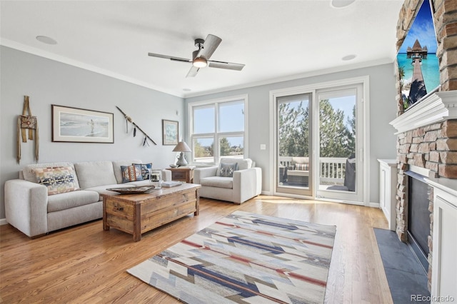 living area featuring ornamental molding, light wood-style floors, a stone fireplace, a ceiling fan, and baseboards