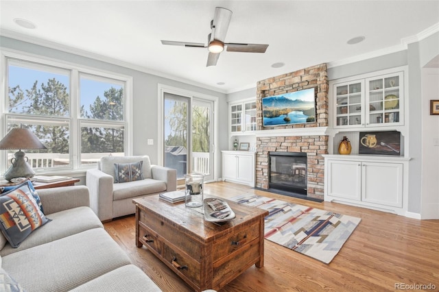 living room with ornamental molding, light wood-style floors, a ceiling fan, a fireplace, and built in features
