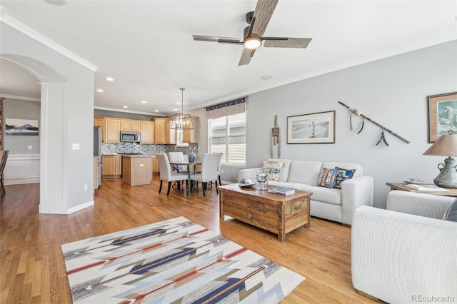 living area with arched walkways, crown molding, light wood-type flooring, a ceiling fan, and recessed lighting