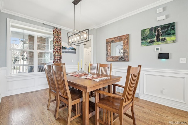 dining area featuring light wood-type flooring, ornamental molding, a chandelier, a decorative wall, and wainscoting