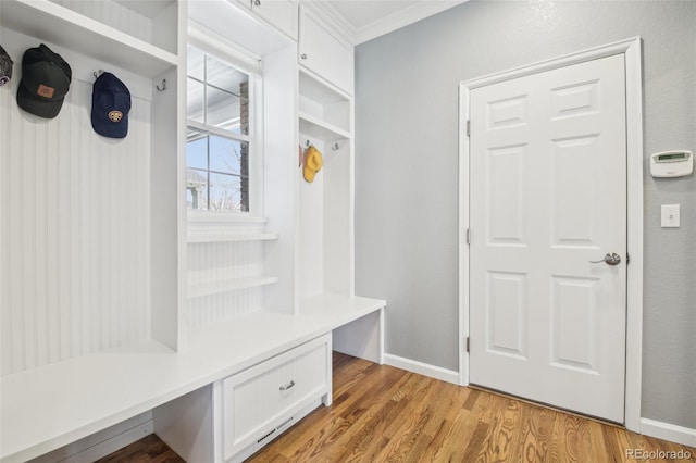 mudroom with crown molding, light wood-type flooring, baseboards, and built in desk