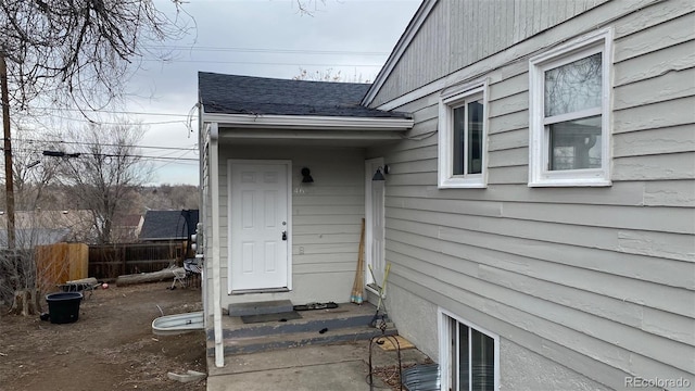 view of exterior entry featuring a shingled roof and fence