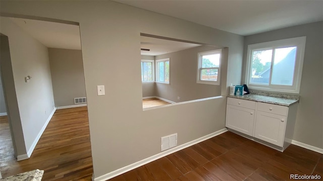 interior space featuring baseboards, dark wood-style flooring, visible vents, and white cabinetry