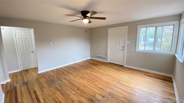 empty room featuring a ceiling fan, baseboards, visible vents, and wood finished floors