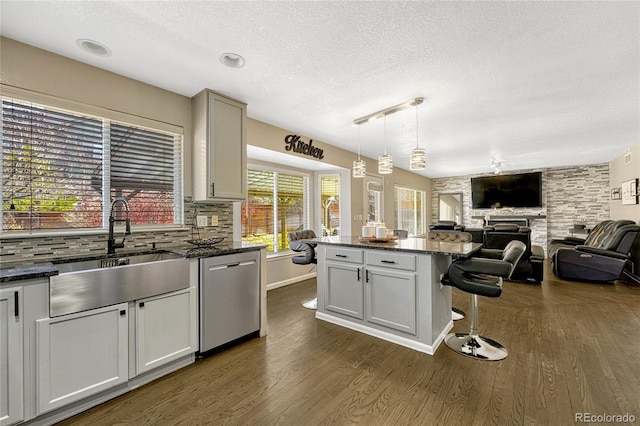 kitchen with pendant lighting, dishwasher, dark stone countertops, a center island, and decorative backsplash