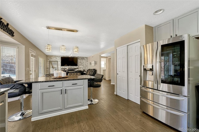 kitchen featuring dark wood-type flooring, a breakfast bar area, dark stone countertops, stainless steel refrigerator, and white cabinets