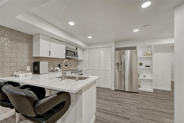 kitchen featuring a breakfast bar, white cabinetry, appliances with stainless steel finishes, kitchen peninsula, and light hardwood / wood-style floors