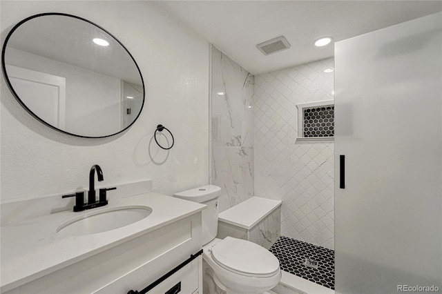 bathroom with tiled shower, vanity, and toilet