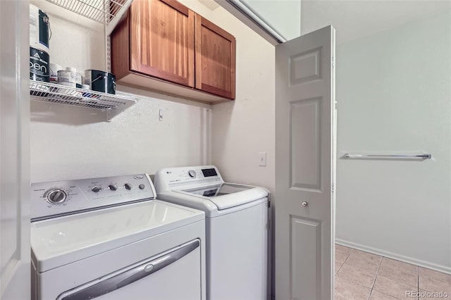 clothes washing area featuring light tile patterned floors, washing machine and dryer, and cabinets