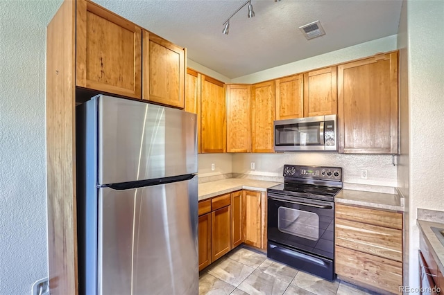 kitchen featuring track lighting, a textured ceiling, stainless steel appliances, and light tile patterned flooring