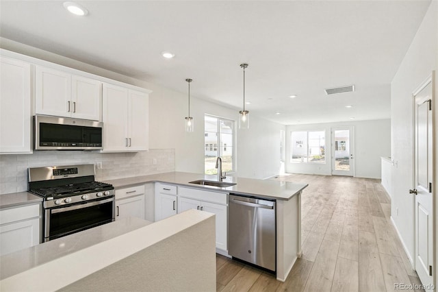 kitchen with hanging light fixtures, light hardwood / wood-style floors, white cabinets, stainless steel appliances, and sink