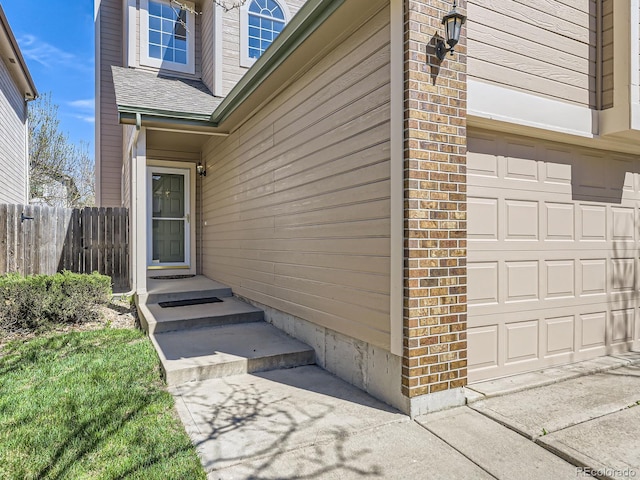 entrance to property with roof with shingles, fence, and a garage