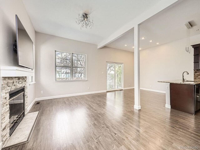 unfurnished living room featuring a fireplace, a sink, baseboards, and wood finished floors