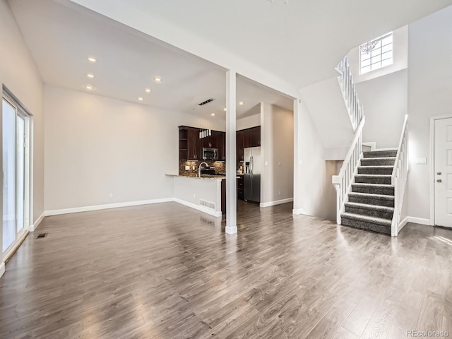 unfurnished living room with stairs, dark wood finished floors, visible vents, baseboards, and recessed lighting