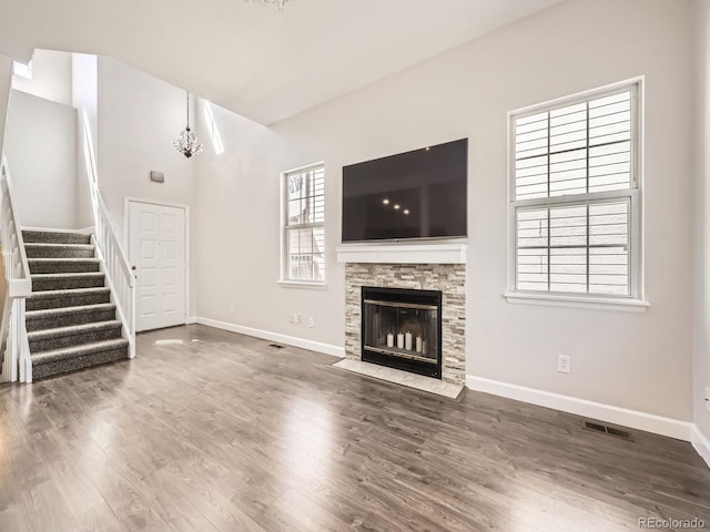 unfurnished living room with wood finished floors, visible vents, baseboards, a chandelier, and stairs
