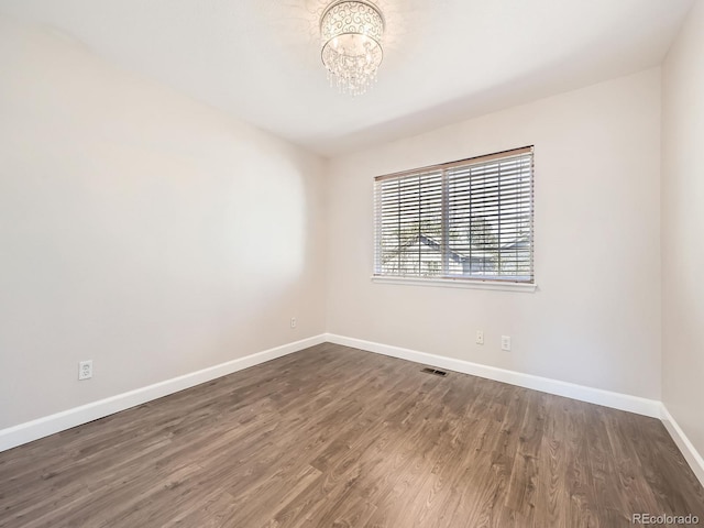 spare room featuring an inviting chandelier, baseboards, visible vents, and wood finished floors