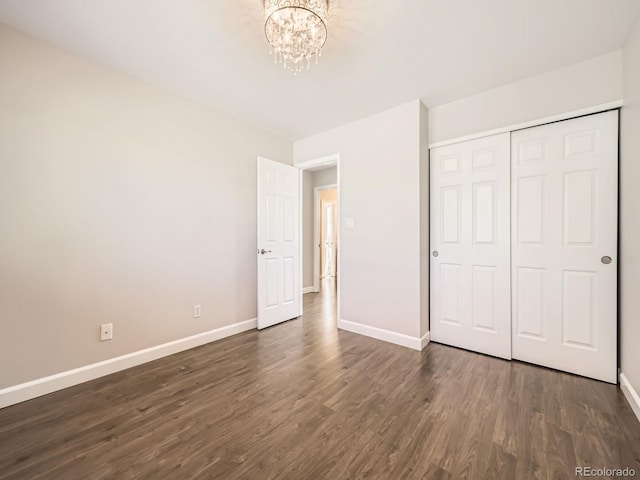 unfurnished bedroom featuring a chandelier, a closet, dark wood-type flooring, and baseboards