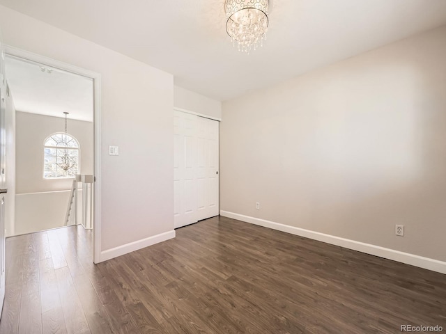 unfurnished room featuring an inviting chandelier, dark wood-type flooring, and baseboards