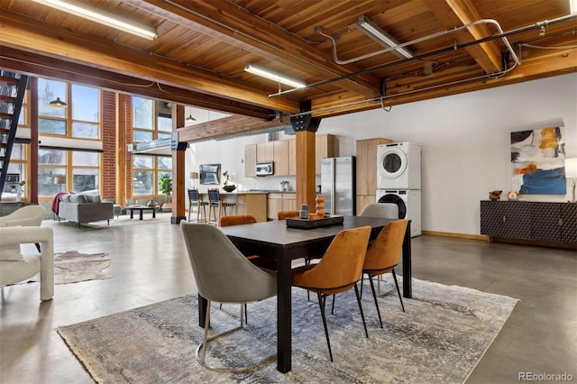 dining room featuring stacked washer / drying machine, beam ceiling, wooden ceiling, and a high ceiling