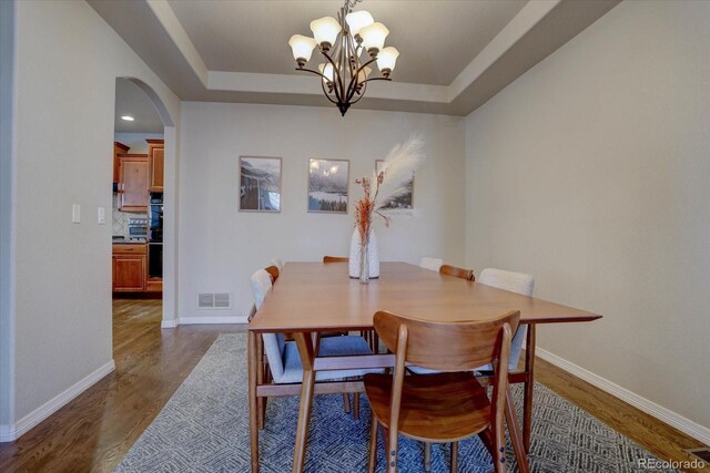 dining area featuring a raised ceiling, dark hardwood / wood-style flooring, and a notable chandelier