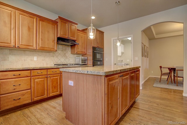 kitchen featuring a center island, light hardwood / wood-style floors, light stone counters, and hanging light fixtures