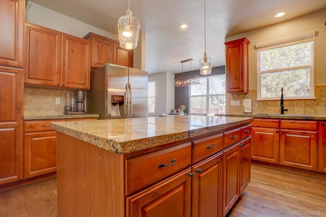 kitchen with stainless steel fridge, a center island, pendant lighting, and light wood-type flooring