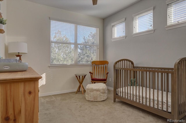 carpeted bedroom featuring multiple windows, ceiling fan, and a crib