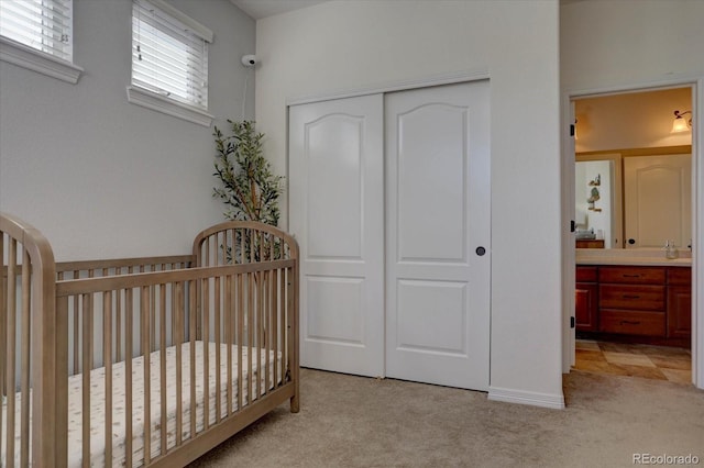 bedroom featuring light carpet, a closet, ensuite bathroom, and a nursery area